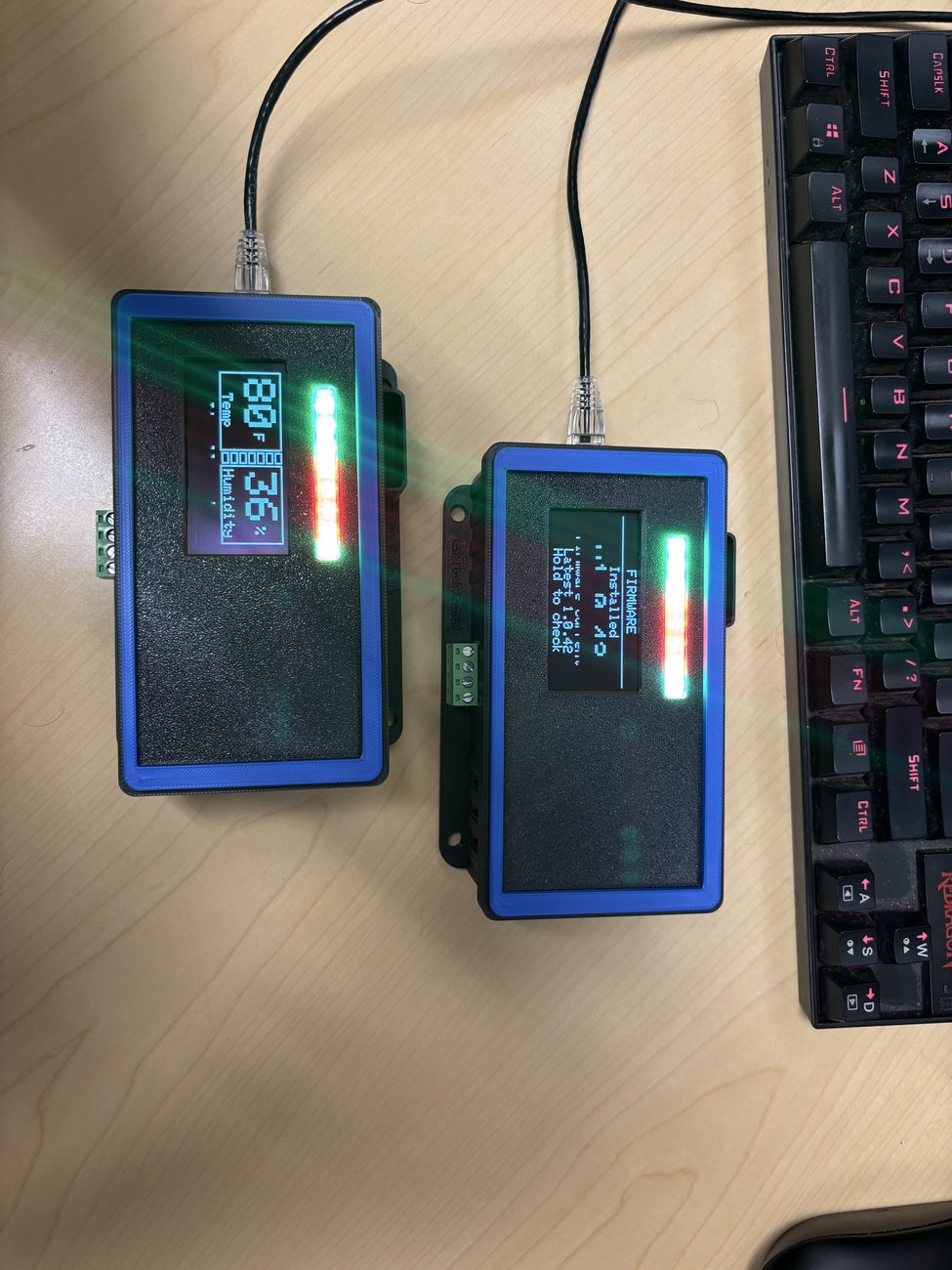 Two small sensor devices with displays and LED status bars on a desk